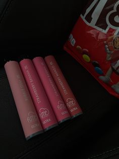 three pink lip balm tubes sitting next to a bag of m & m candy