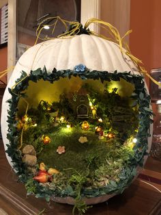 a white pumpkin decorated with fairy lights and greenery in the shape of a house