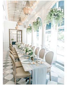 a long dining table set with white flowers and greenery on the tables for an elegant wedding reception