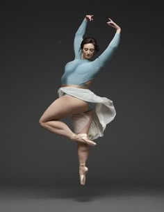 a woman in a blue top and white skirt is doing a dance pose with her hands up