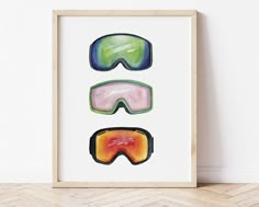 three ski goggles are displayed in a frame on the floor next to a wall