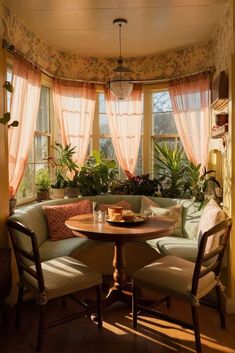 a corner table with two chairs around it in front of a window filled with plants