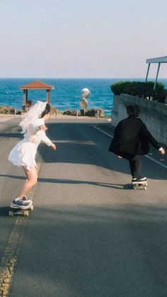 two people riding skateboards down a street next to the ocean