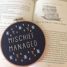 an embroidered book with the words mischef managed on it next to a cross stitch hoop