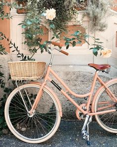 an orange bicycle parked next to a wall with flowers growing on it's side