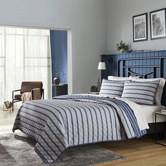 a bed with blue and white striped comforter in a bedroom next to a window