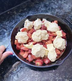 a pan filled with food sitting on top of a counter next to a person's hand