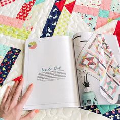 a woman's hand is holding an open book on top of a quilted blanket