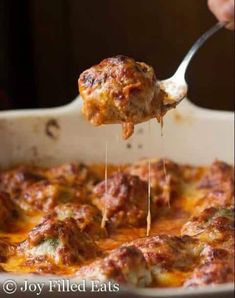 a person holding a spoon full of food with meat and cheese on it in a casserole dish