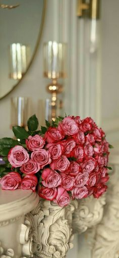 a bouquet of pink roses sitting on top of a white pedestal next to a mirror