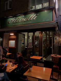 people sitting at tables in front of a restaurant with the name cittabelli on it