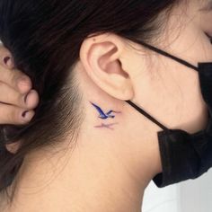 a woman's neck with a bird tattoo on her left side behind the ear