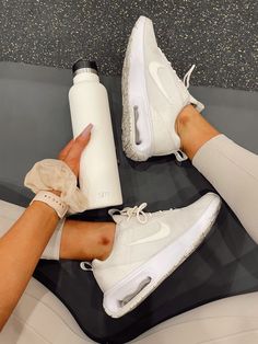 a woman's legs with white shoes and a water bottle on her lap, both holding the same item