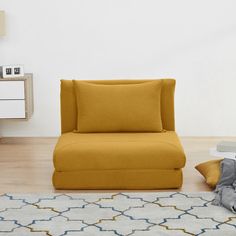 a yellow chair sitting on top of a wooden floor next to a white dresser and lamp