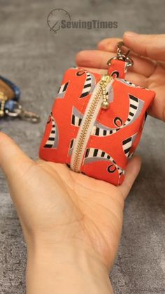 a hand is holding an orange and black zippered pouch with two keys in it