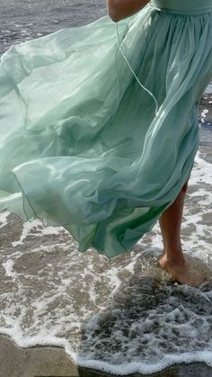 a woman in a green dress is walking on the beach