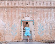 a woman in a blue dress standing at the entrance to a building with painted flowers on it