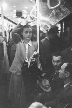 an old black and white photo of people on a subway train, looking at something in the distance