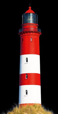 a red and white lighthouse sitting on top of a grass covered hill next to the ocean