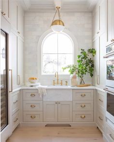 a kitchen with white cabinets and gold hardware on the countertop, an arched window above the sink