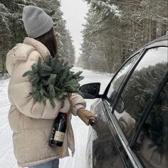 a woman is holding a christmas tree in her hand and getting out of the car