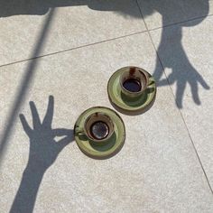 two coffee cups sitting on top of saucers next to each other in front of a person's shadow