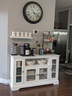 a clock mounted on the wall above a white cabinet with glass doors and shelves filled with dishes