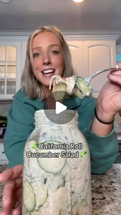 a woman holding a jar with cucumber salad in it