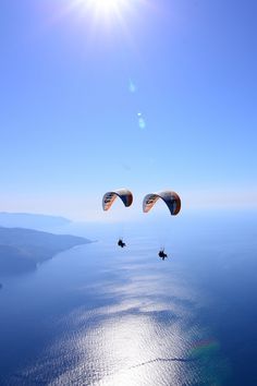 two people parasailing over the ocean under a blue sky with sun flares