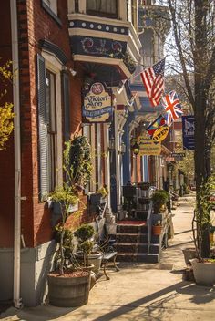 an american flag hanging from the side of a building on a city street with potted plants