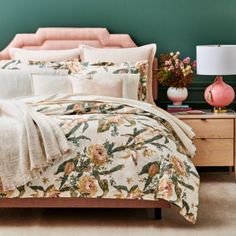 a bed with floral comforter and pillows in a green room next to a pink lamp