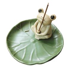 a frog figurine sitting on top of a leaf with a stick in it's mouth