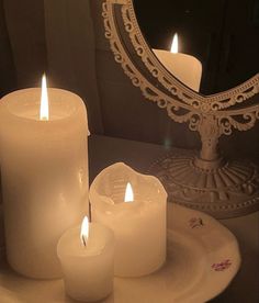 three lit candles sit on a plate in front of a mirror with an ornate frame