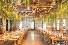 an indoor venue with tables and chairs covered in greenery, surrounded by hanging lights