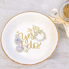 two wedding rings on a white plate with the words yes to do in gold lettering