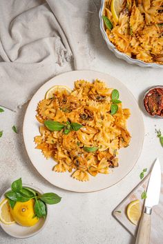 a white plate topped with pasta next to a bowl of lemons and basil leaves