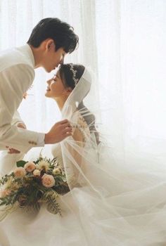 a bride and groom kissing in front of a window