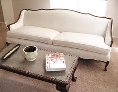 a white couch sitting on top of a table next to a book and cup with a pen