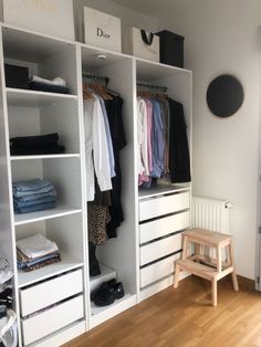 a white closet filled with clothes and other items on top of wooden flooring next to a wall mounted clock