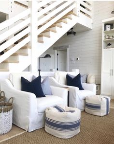 a living room with white furniture and blue pillows on the floor next to a stair case