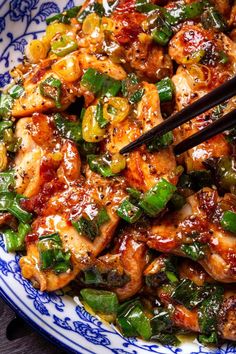 a blue and white plate topped with chicken, peppers and onions next to chopsticks