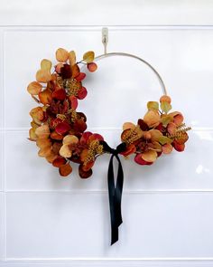 a wreath with orange and red flowers hanging on a white wall next to a black ribbon