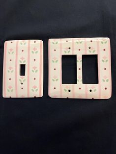 two pink and green striped switch plates on a black surface with white flowers in the center