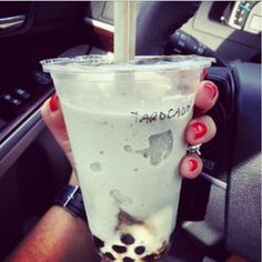 a woman holding up a drink in her hand while sitting in the drivers seat of a car