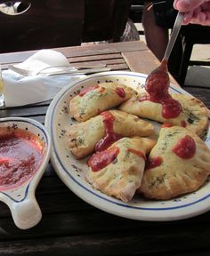 a plate full of pastries and dipping sauces on a table with two glasses of wine