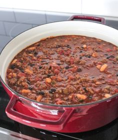 a red pot filled with chili sitting on top of a stove