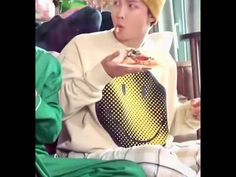 the boy is eating pizza while wearing a yellow hat and holding a black bag in his hand