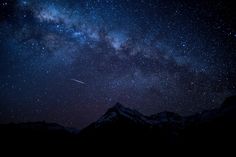 the night sky is filled with stars, and there are mountains in the foreground