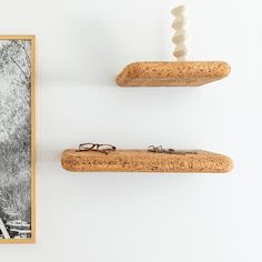 two corks are hanging on the wall next to a framed photograph with glasses sitting on them