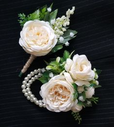 two white flowers and pearls are on a black surface with some green leaves in the middle